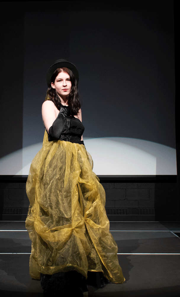 A young woman in a black sleeveless shirt dress and a gold skirt.