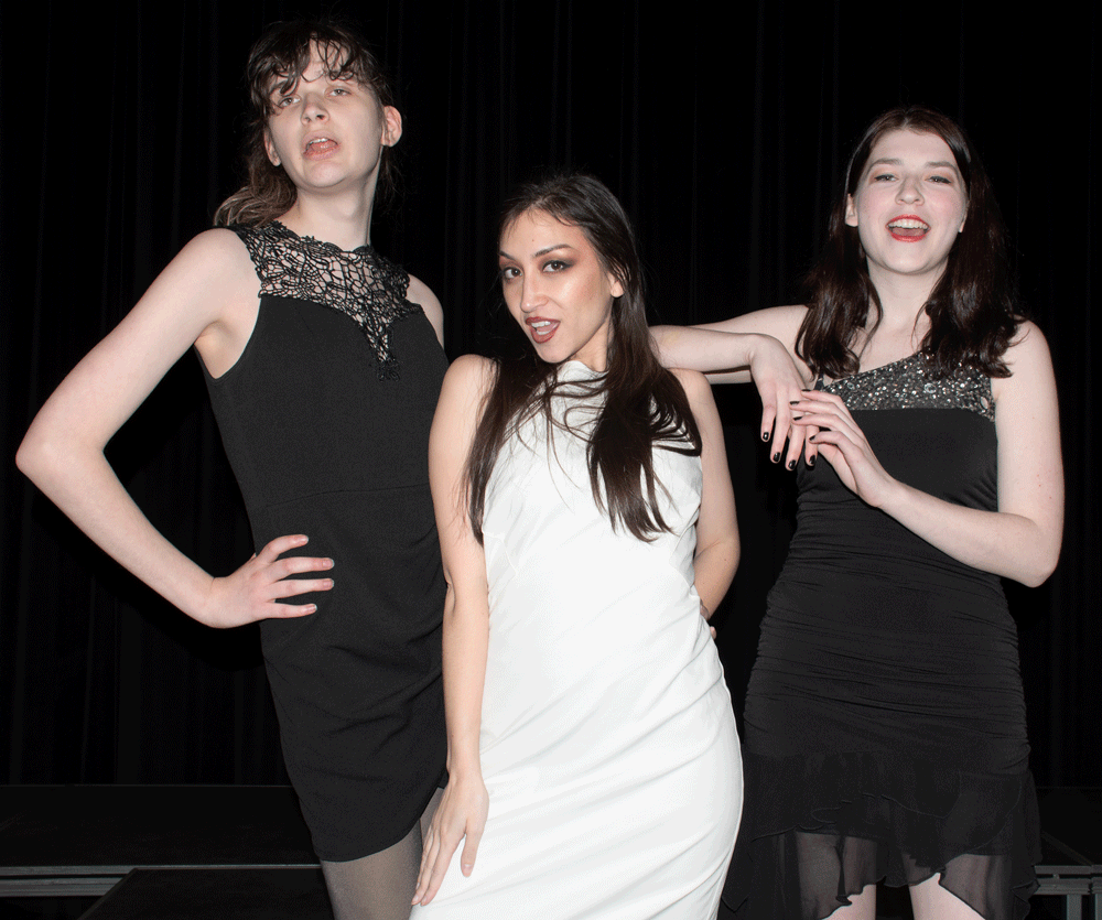 Three female models, two dressed in black and one dressed in white, posing together.