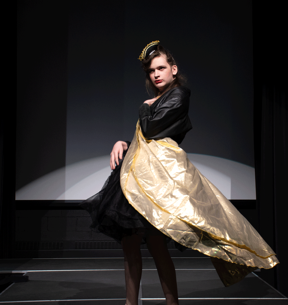 A tall woman in a black dress with a gold cape.