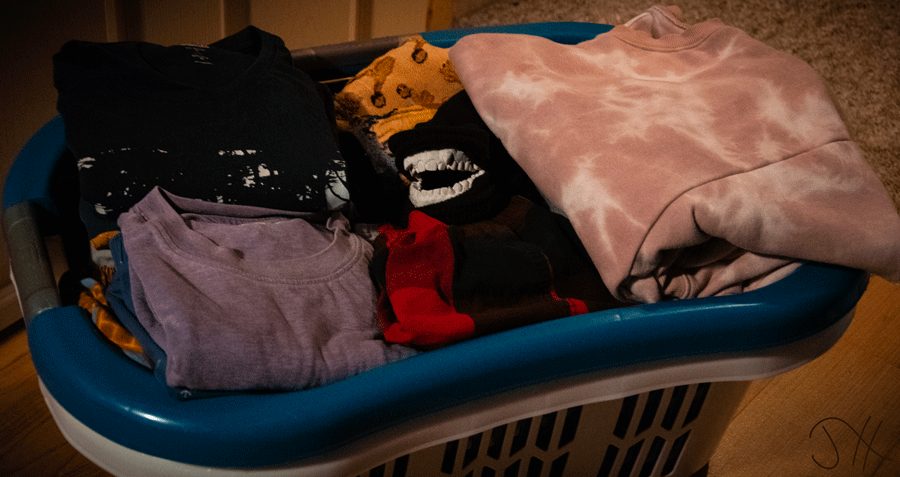 A laundrey basket full of folded clothes, with a model of human teeth hiding in the sleeve of a sweater.