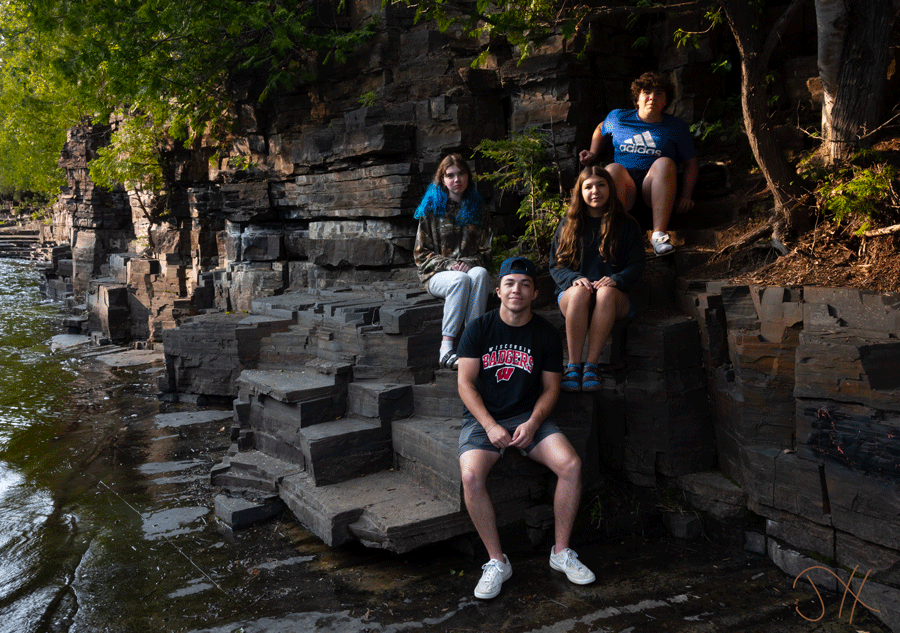 Four teenagers sitting on some rocks next to a shallow river.