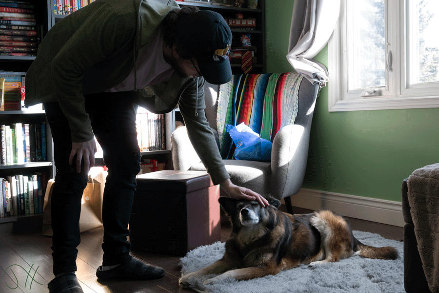 A photograph of a tall man leaning down to pat his dog on the head.