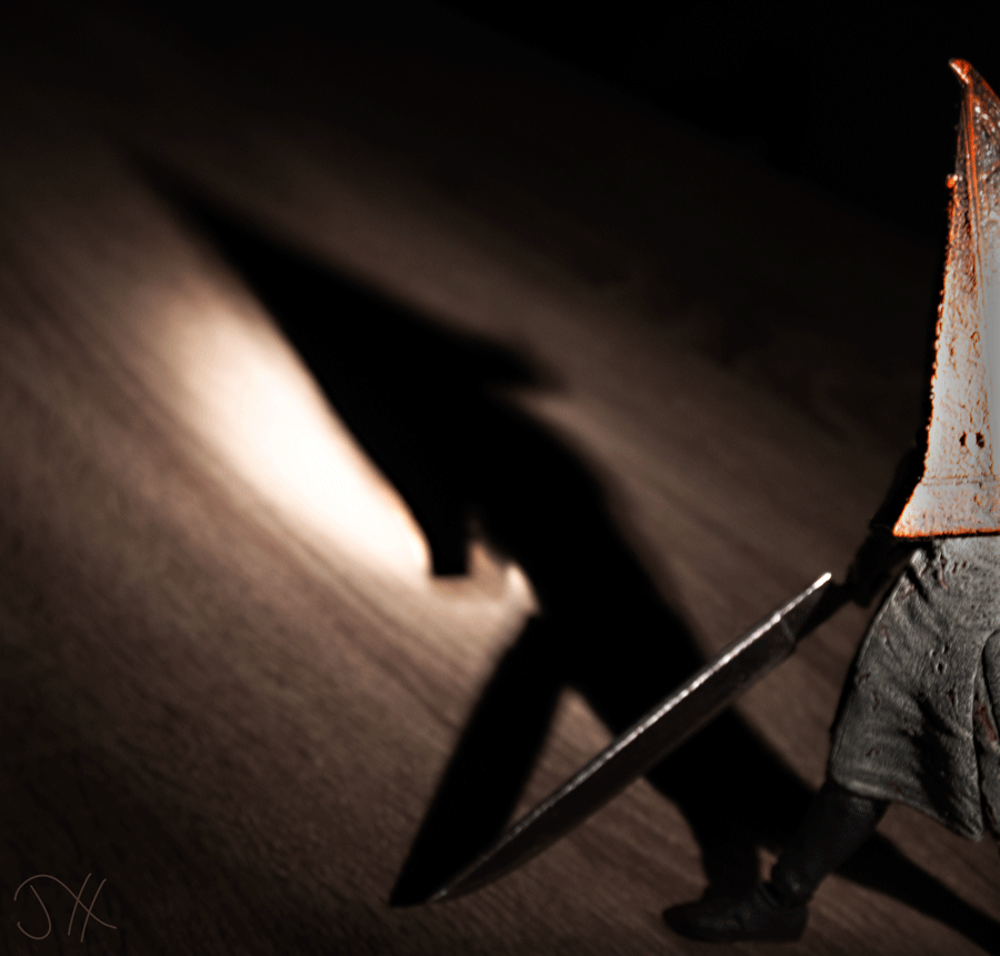 A figurine of Pyramid Head from Silent Hill 2 with its shadow spread across the floor behind it.